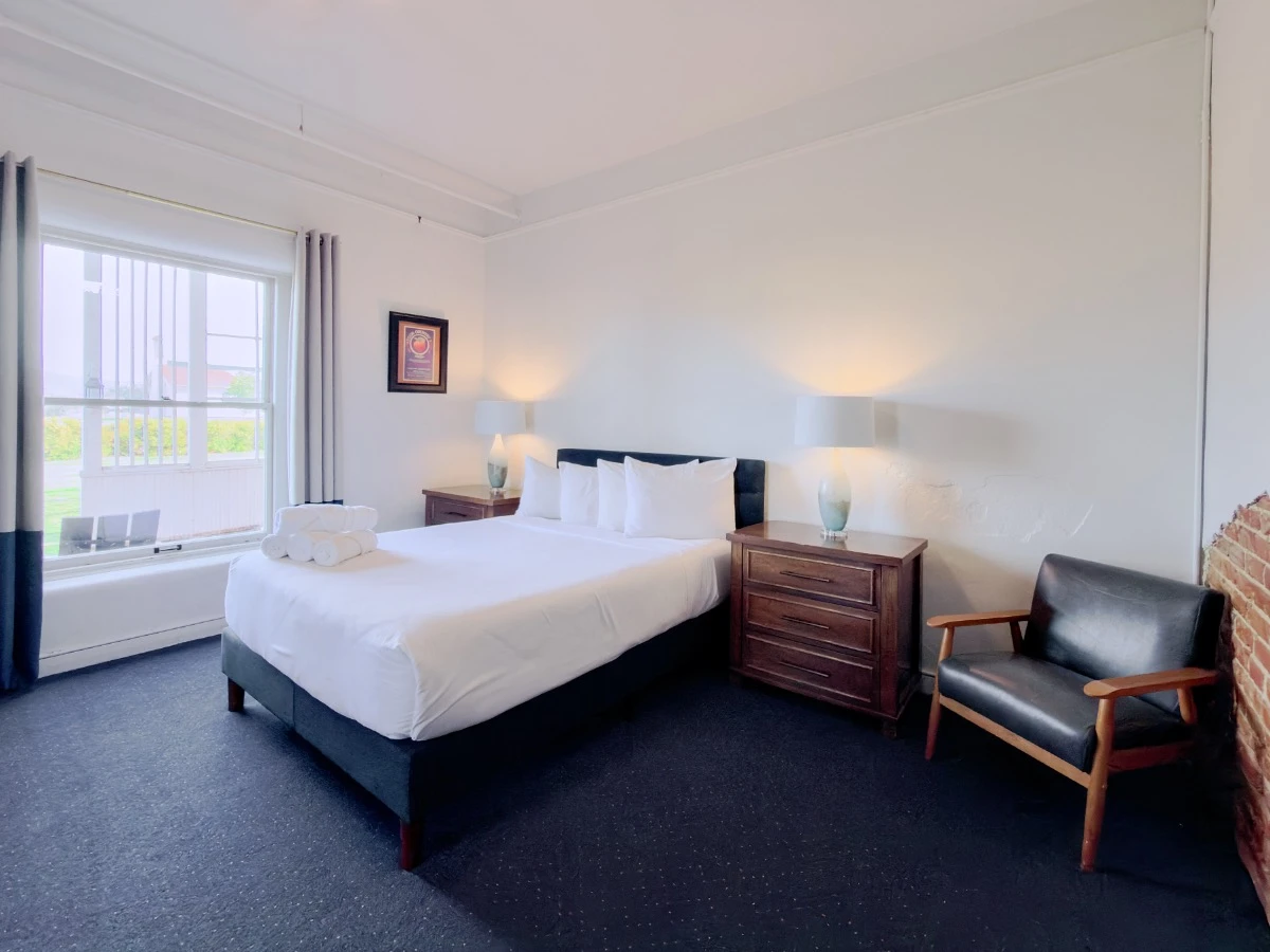 Bed with single window, dark nightstands with lit lamps, and single chair in Room 113 at Hot Lake Springs Resort.