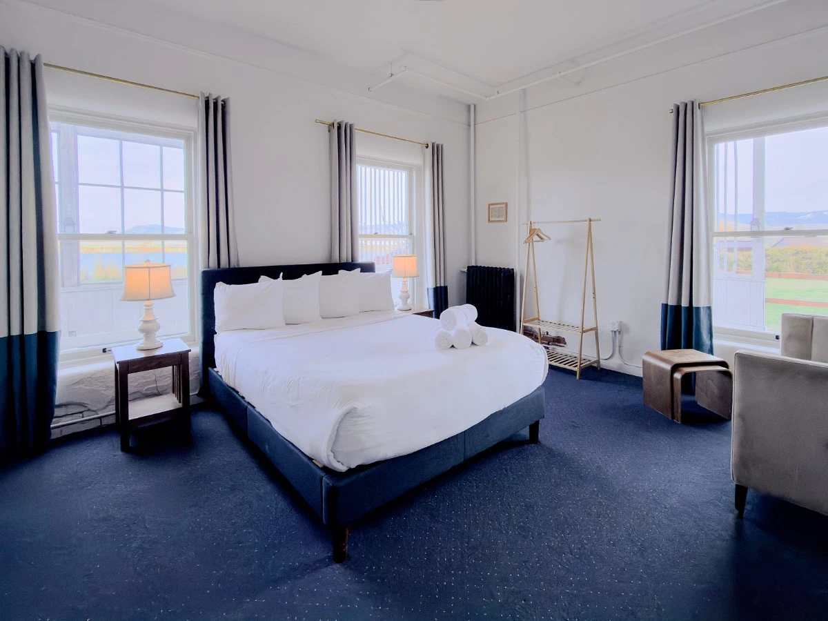 Bed with nightstands and windows in Room 113 at Hot Lake Springs Resort, sofa and coffee table partially visible on right.