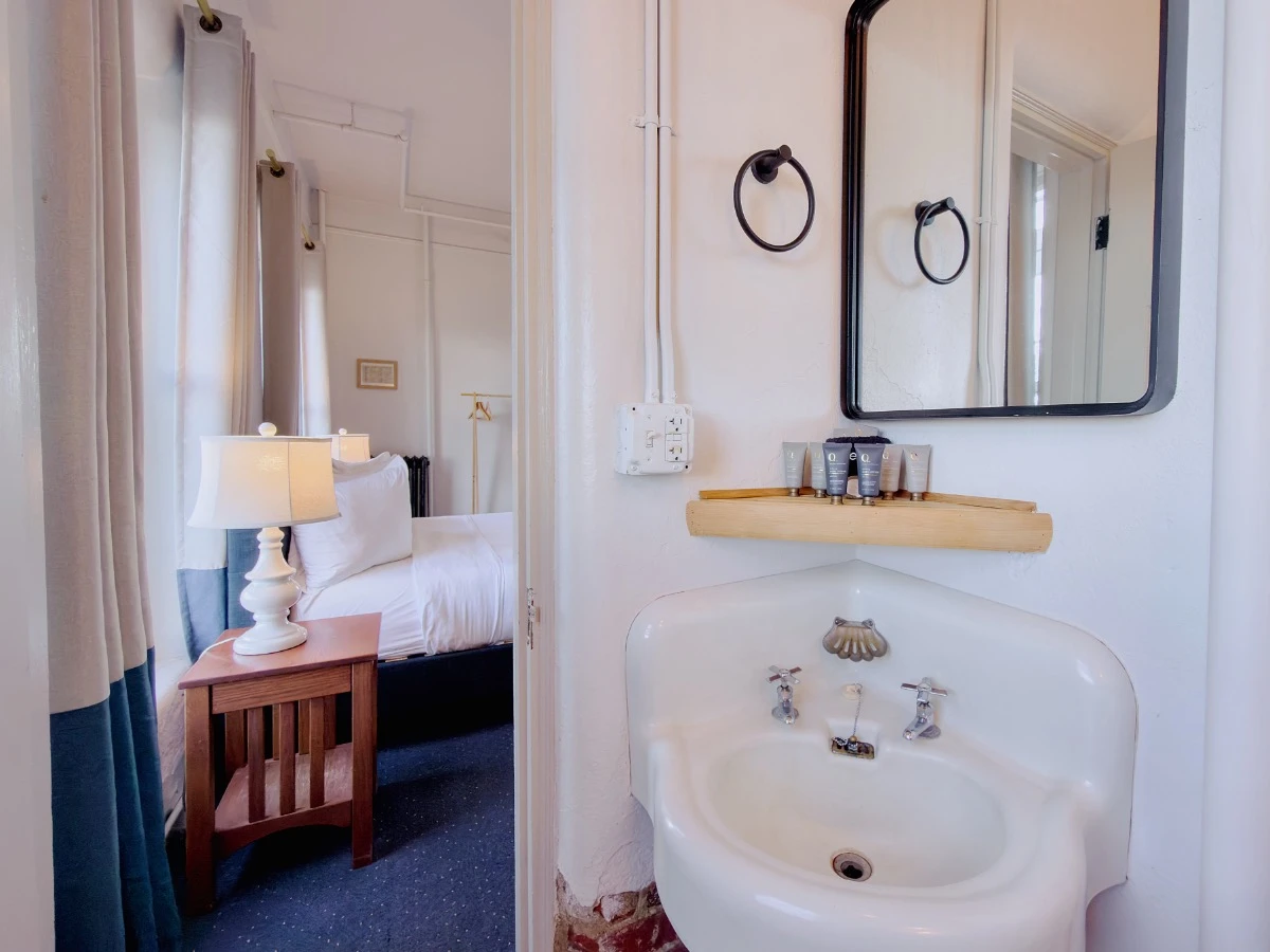 View from inside bathroom of Room 113 at Hot Lake Springs Resort, corner sink with mirror on right and partial bed view through doorway.