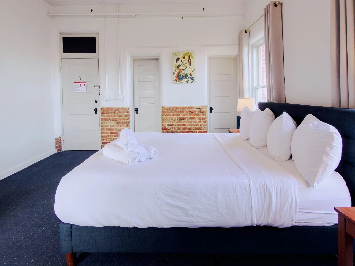 Bed in foreground of Room 113 at Hot Lake Springs Resort with three closed doors visible in the background.