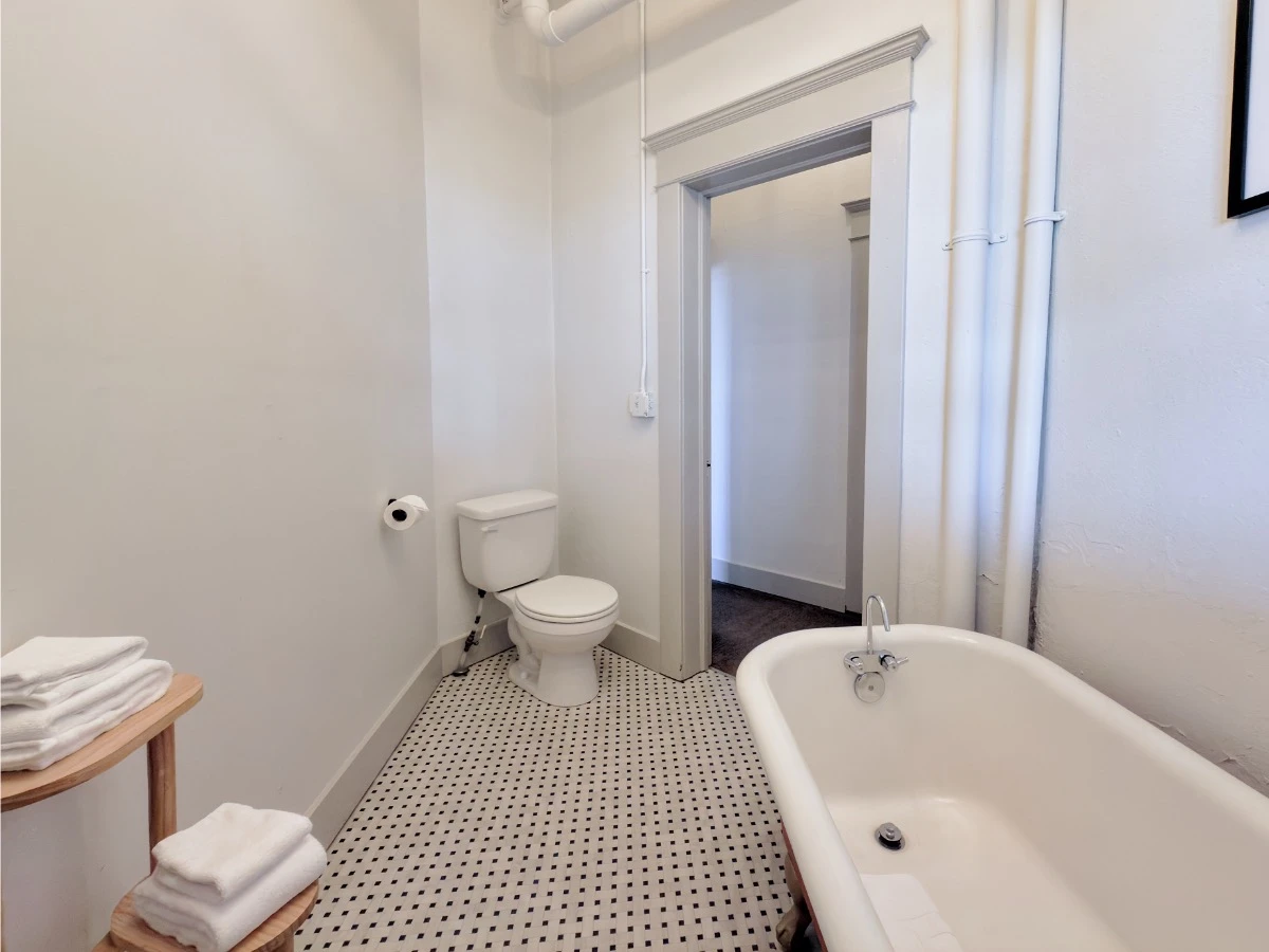 View from bathroom in Room 115 at Hot Lake Springs Resort, clawfoot soaking tub in foreground on right, toilet on left, black and white flooring.