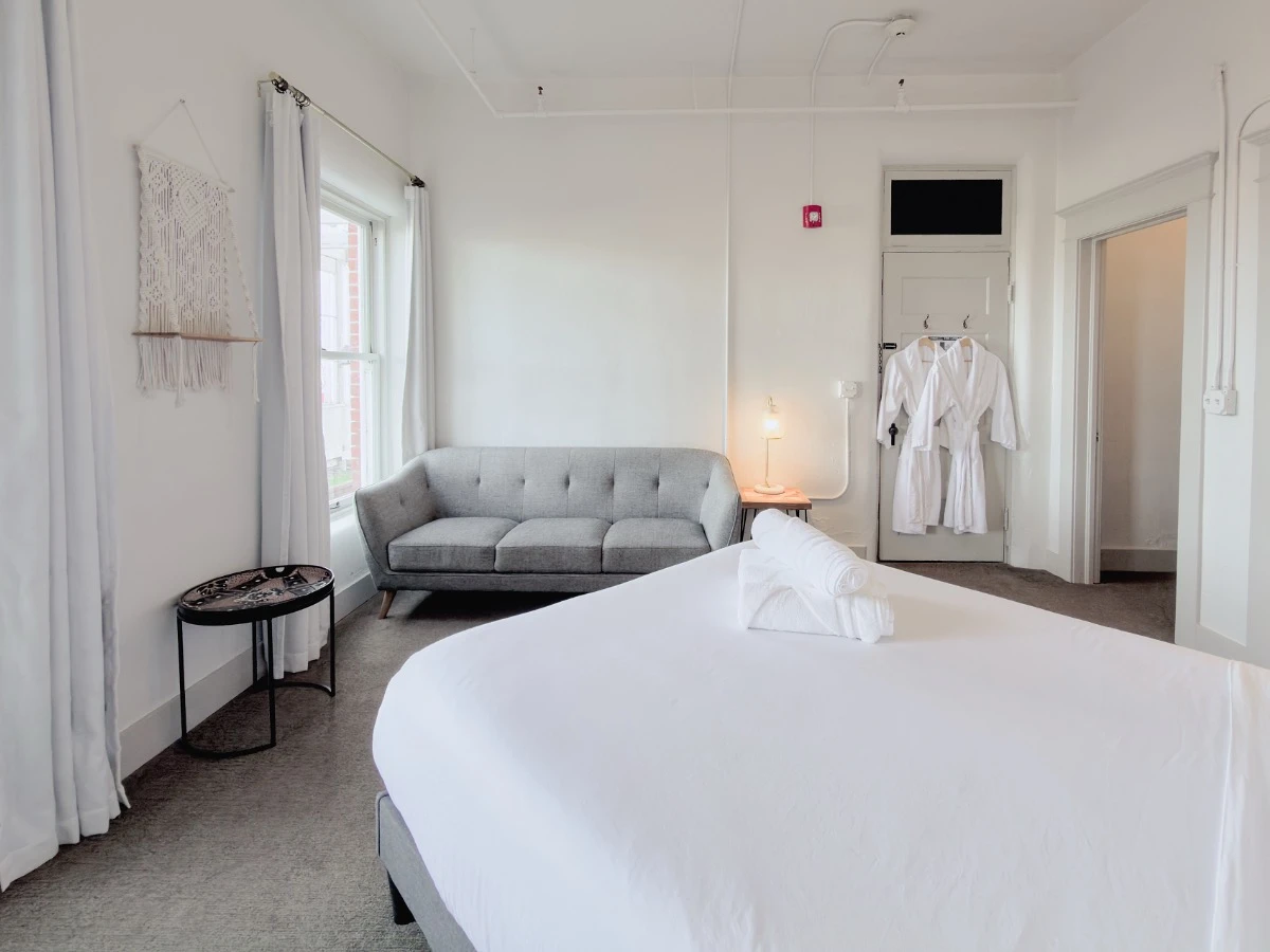 View across foot of bed in Room 115 at Hot Lake Springs Resort showing grey sofa, end table and window.