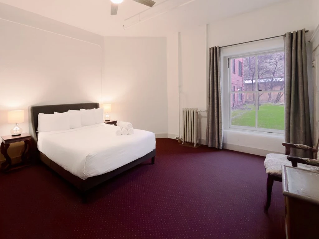 Bed with two nightstands and lit lamps in Room 118 at Hot Lake Springs Resort, window on right showing courtyard, grey curtains open.