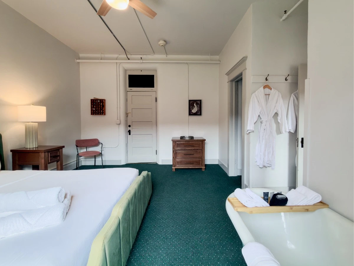 View across bed and clawfoot tub in Room 202 at Hot Lake Springs Resort, single seat on left and small 3-drawer dresser on right against far wall.