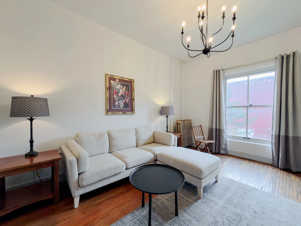 Living room in Room 202 at Hot Lake Springs Resort with grey sofa, end tables and lit lamps on each side, round black coffee table, and window in background.