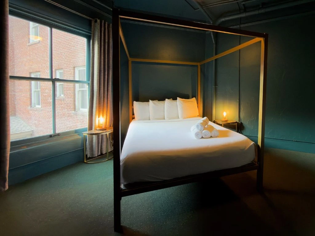 Bed in Room 206 at Hot Lake Springs Resort with window to the left letting in natural light mixed with glow from nightstand lamps.