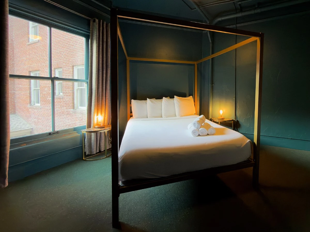 Bed in Room 206 at Hot Lake Springs Resort with window to the left letting in natural light mixed with glow from nightstand lamps.