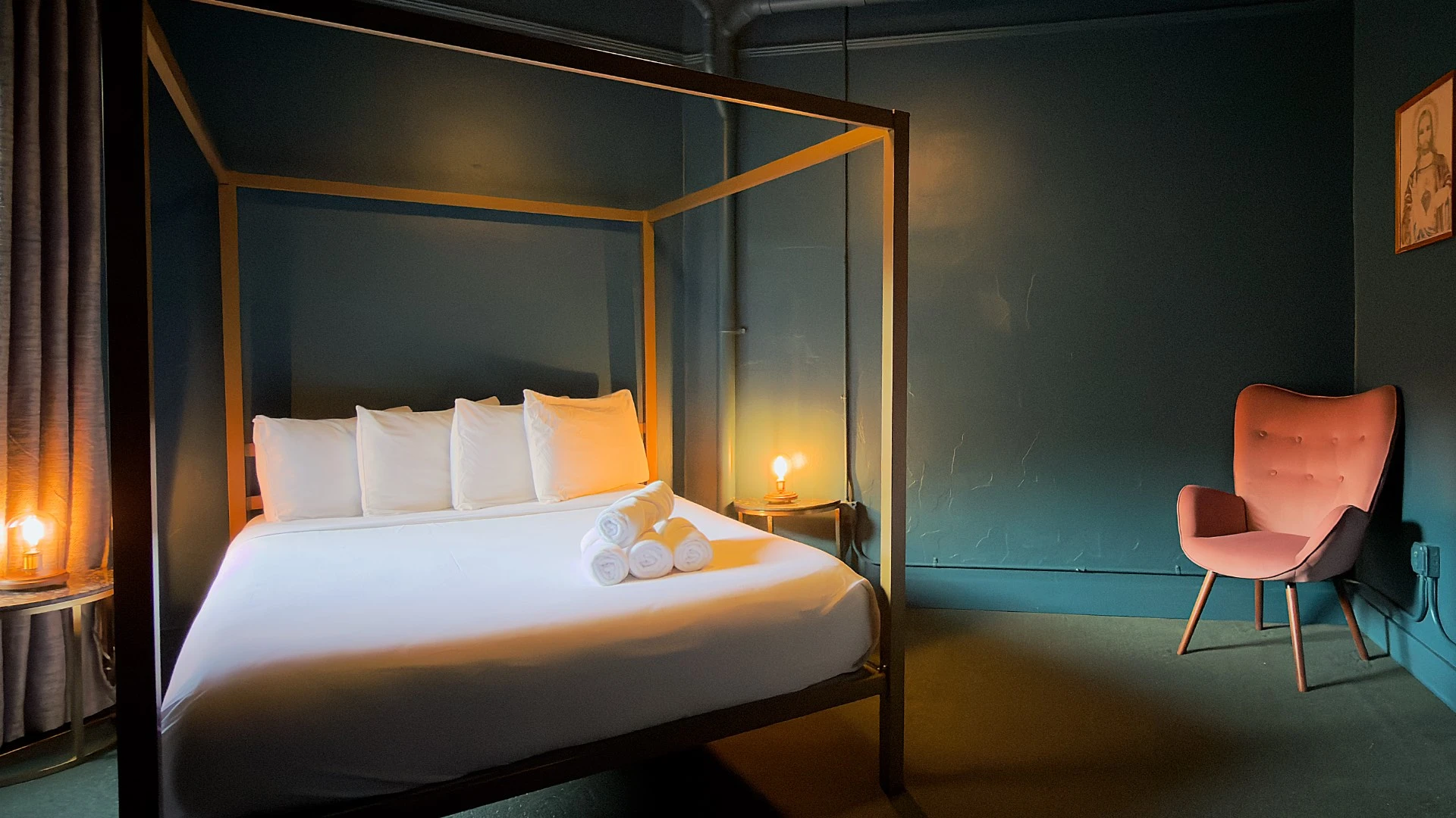 Bedroom in Room 206 at Hot Lake Springs Resort with bed on left, nightstands and lit lamps on each side, orange chair in right back corner, dark green carpet and dark blue/green walls.