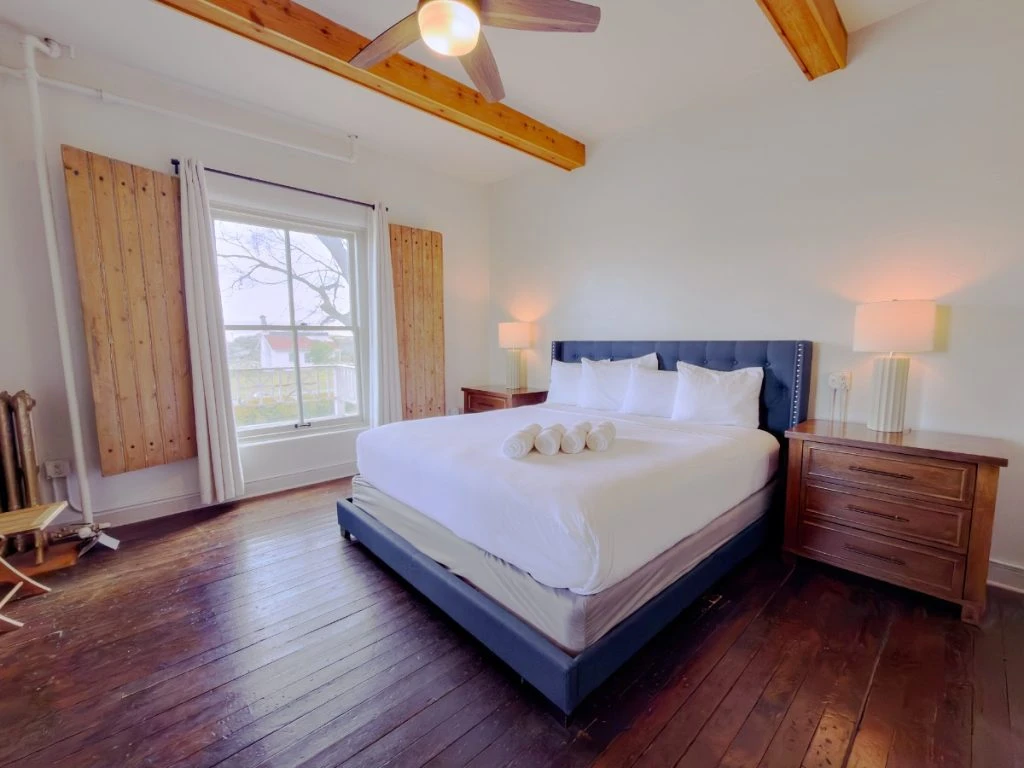 Bed with blue frame and headboard in Room 213 at Hot Lake Springs Resort, wood nightstands with lit lamps on each side, window across from bed.