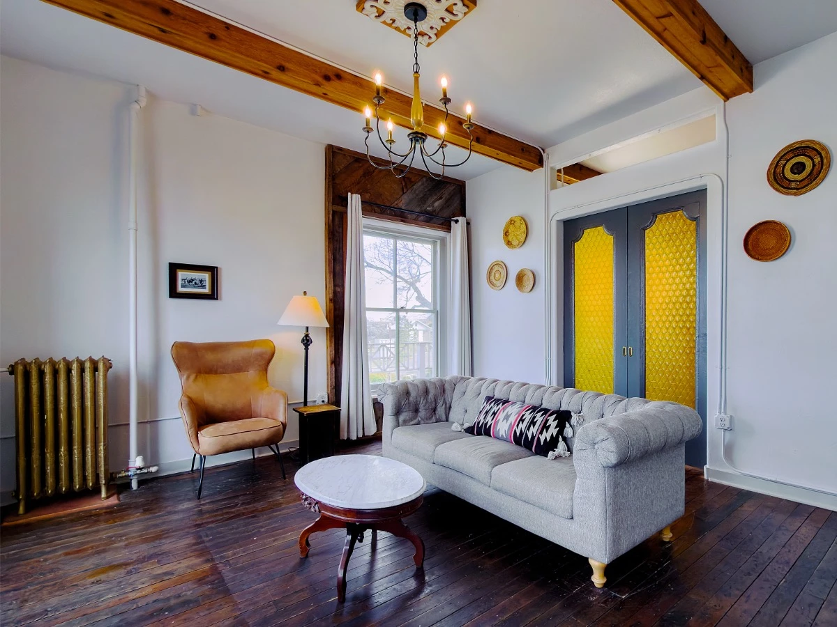 Front of grey sofa in Room 213 at Hot Lake Springs Resort with closed sliding doors to bedroom glowing gold, window to the left of doors, single sitting chair to the left of window, marble coffee table in front of couch.