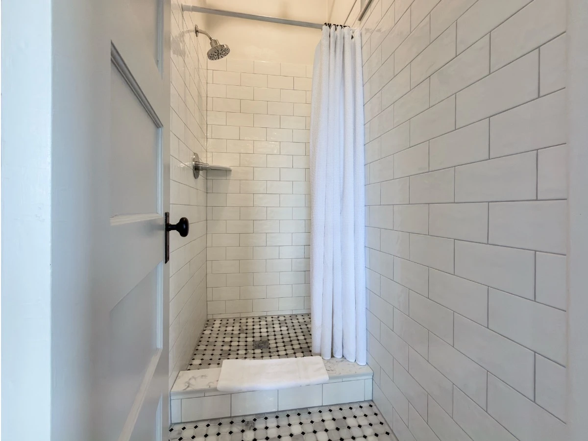 Tiled white shower in Room 213 at Hot Lake Springs Resort with shower curtain pulled back and small step up into shower.