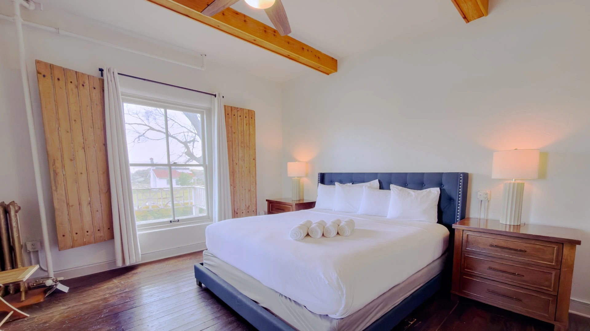 Bed with blue frame and headboard in Room 213 at Hot Lake Springs Resort, wood nightstands with lit lamps on each side, window across from bed.