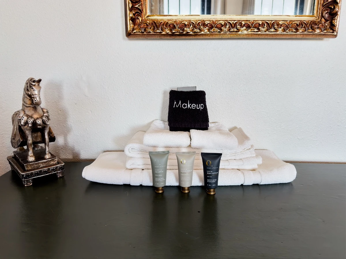 Close-up of olive desk in Room 223 at Hot Lake Springs Resort with toiletries, neatly folded washcloths and hand towel, shampoo, conditioner, lotion, and silver horse figurine to the left.