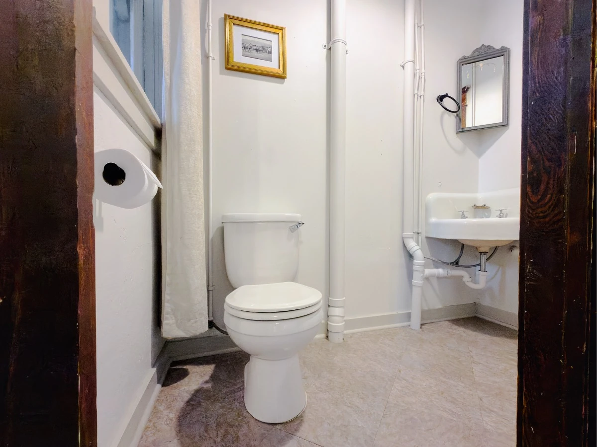 Bathroom in Room 224 at Hot Lake Springs Resort showing toilet on left and corner hand sink with mirror above on right.