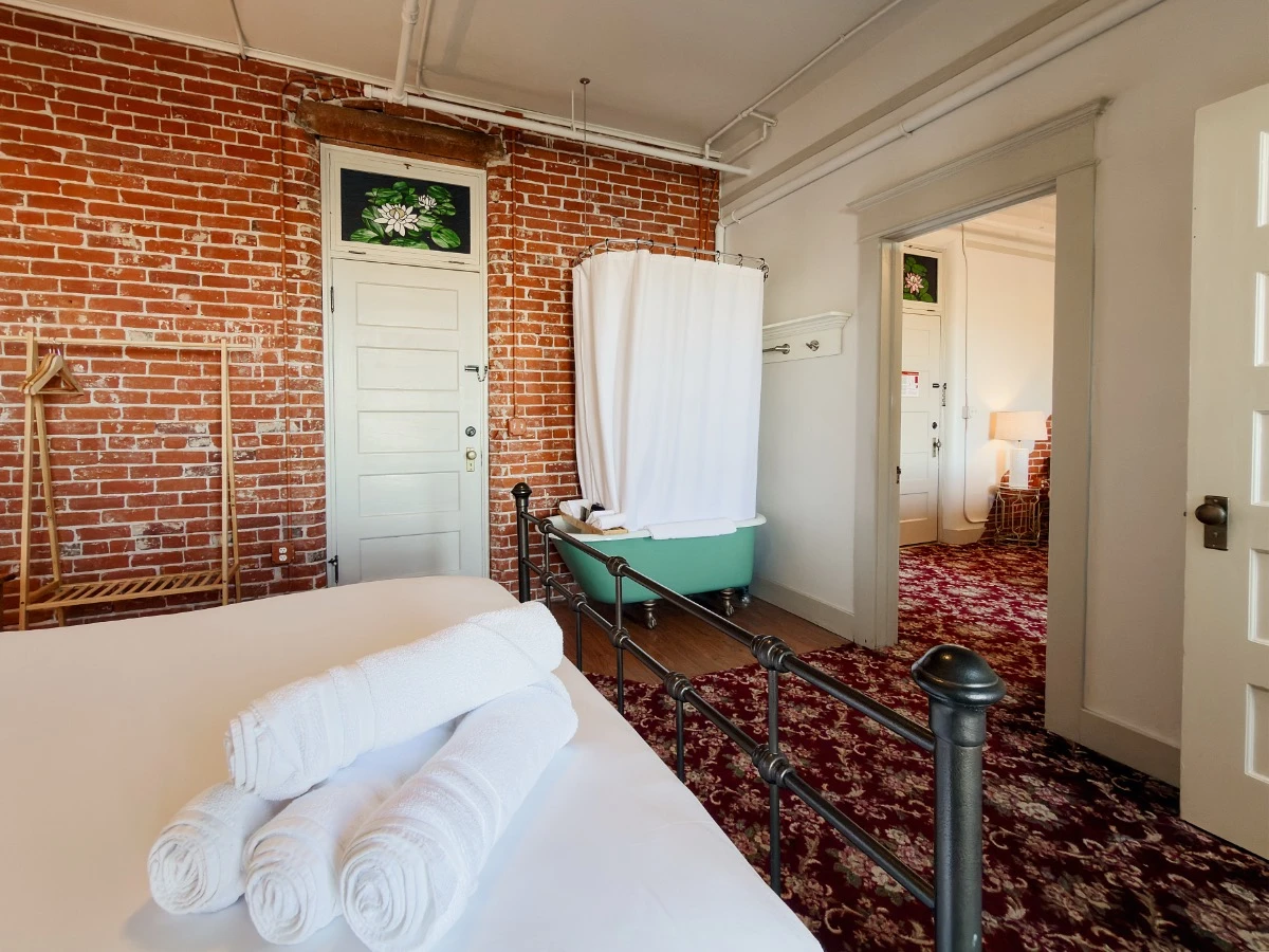View across bed in Room 227 at Hot Lake Springs Resort toward in-room clawfoot soaking tub and doorway to living room.