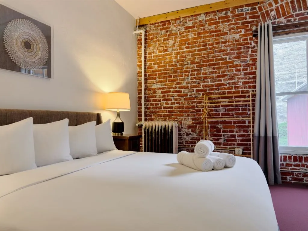 View across foot of bed in Room 324 at Hot Lake Springs Resort at red brick wall and partial view of window.