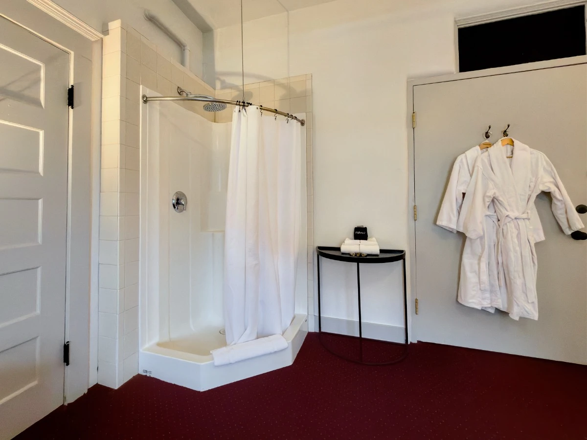 Corner shower in bedroom of Room 324 at Hot Lake Springs Resort with two white bathrobes hanging to the right of the shower.