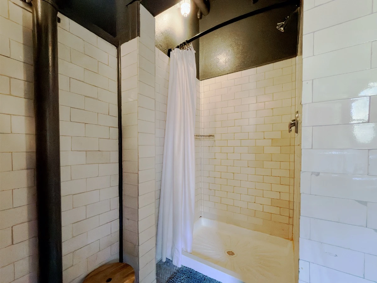 Closer interior view of shared shower stall with open curtain in historic lodge shared bathroom at Hot Lake Springs Resort.