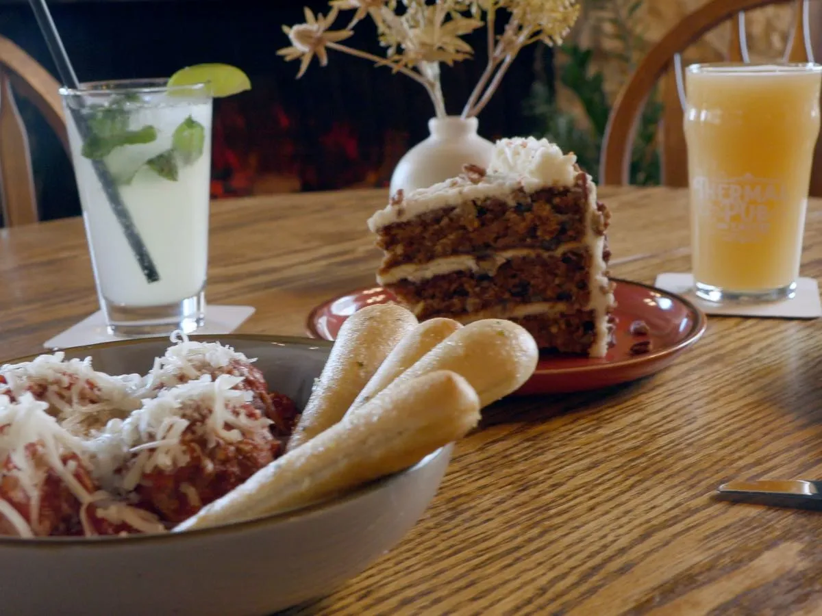 Close-up table setting at Thermal Pub & Eatery: frosty beer, muddled mint drink, meatballs with breadsticks and marinara, and carrot cake.