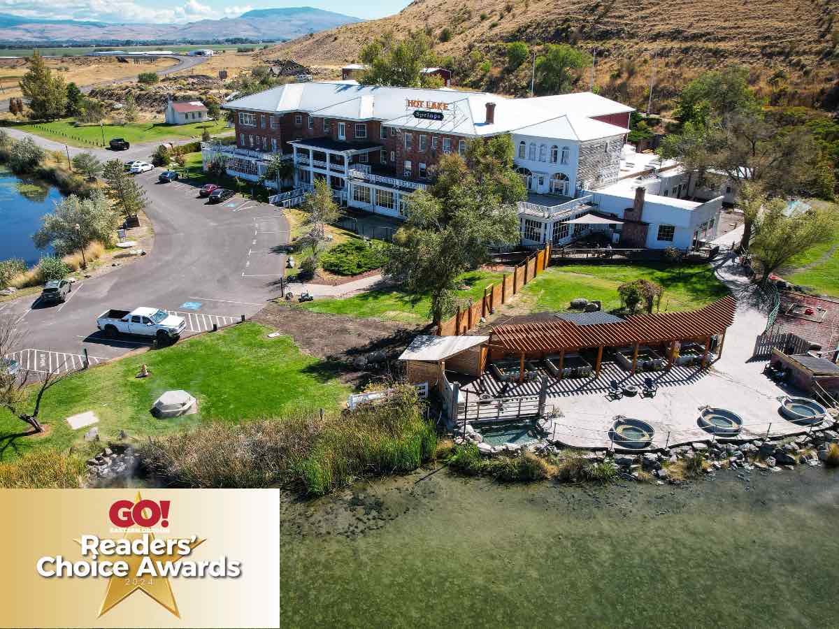 Aerial summer view of Hot Lake Springs Resort showing the building, parking, soaking area, and Go Magazine Readers' Choice Awards icon in the lower left.