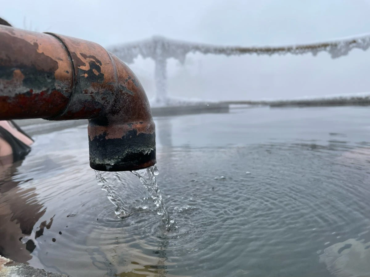 Frosty morning at Hot Lake Springs Resort, ice on safety ropes, copper faucet filling round soaking tub with running hot water.