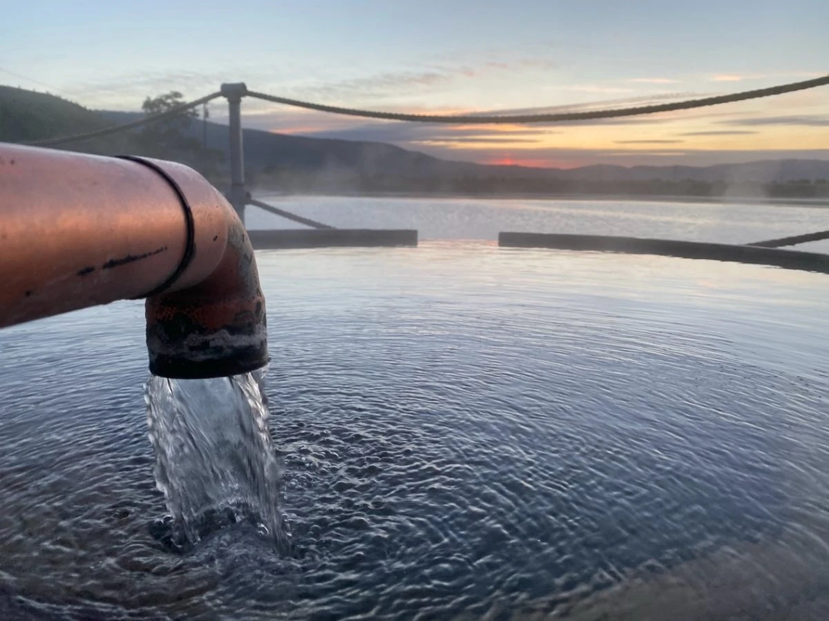 Copper faucet filling round soaking pool at Hot Lake Springs Resort, Hot Lake and simple sunset in background.