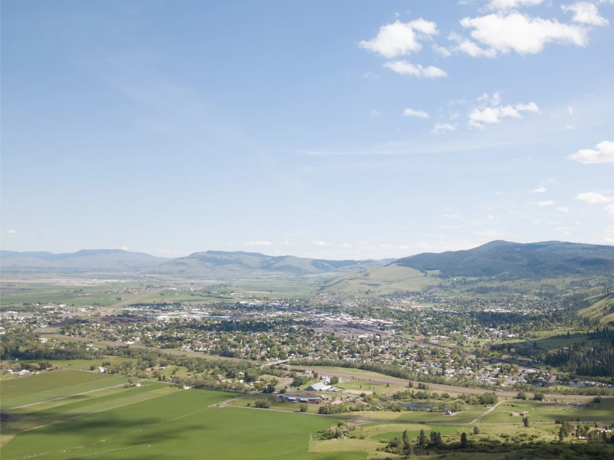 Panoramic view of La Grande Valley from mountain overlook, showing Blue Mountains, city of La Grande, and expansive Union County landscape under sunny blue skies.