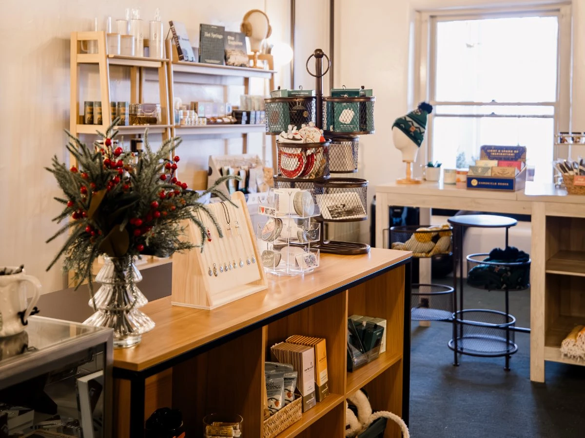 Interior of Gift Shop at Hot Lake Springs Resort, showing counter display, table with stickers, hats, jewelry, lip balm, and assorted keepsakes.