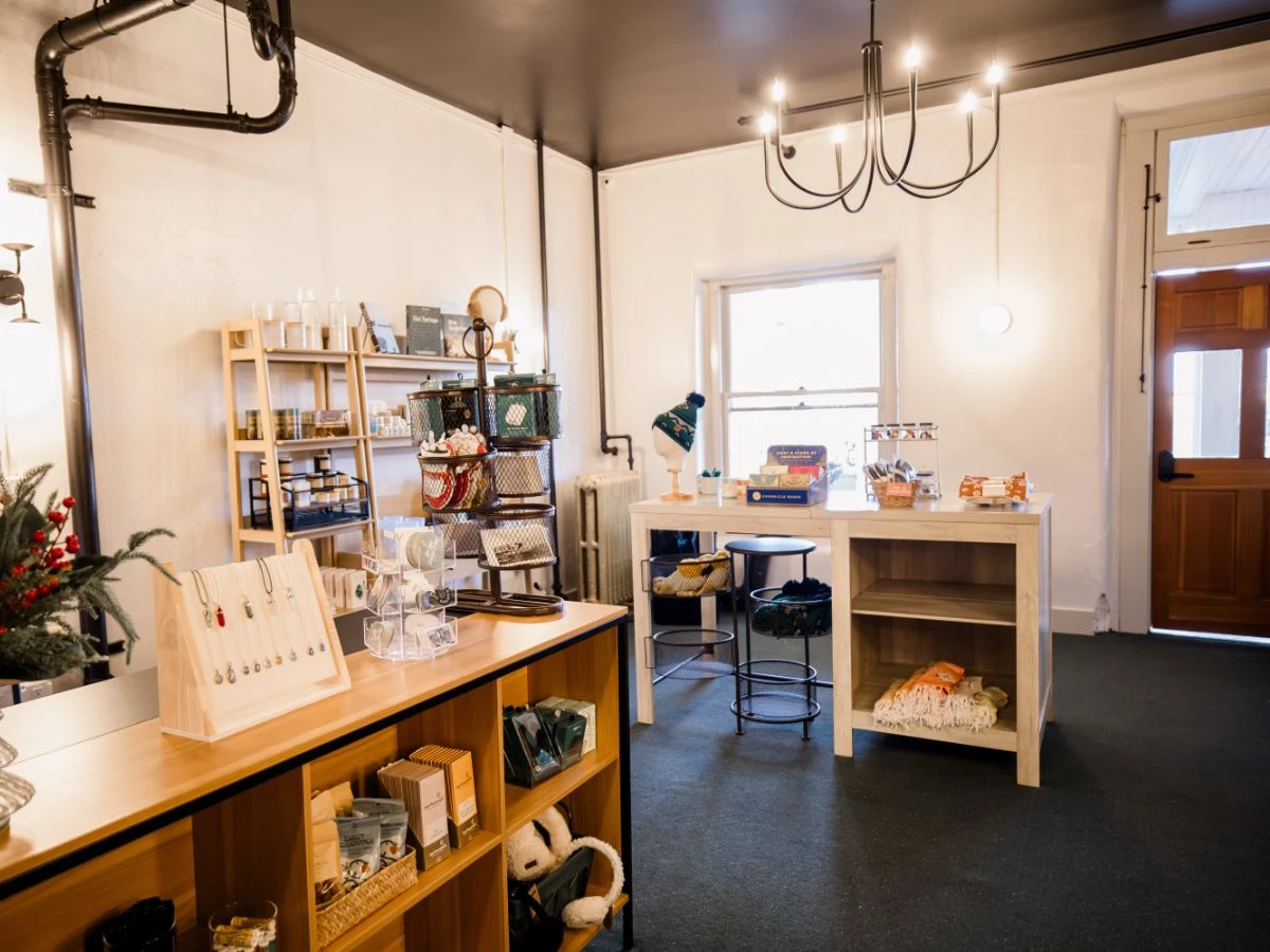 Interior of Gift Shop at Hot Lake Springs Resort, showing counter display, table with stickers, hats, jewelry, lip balm, and assorted keepsakes.