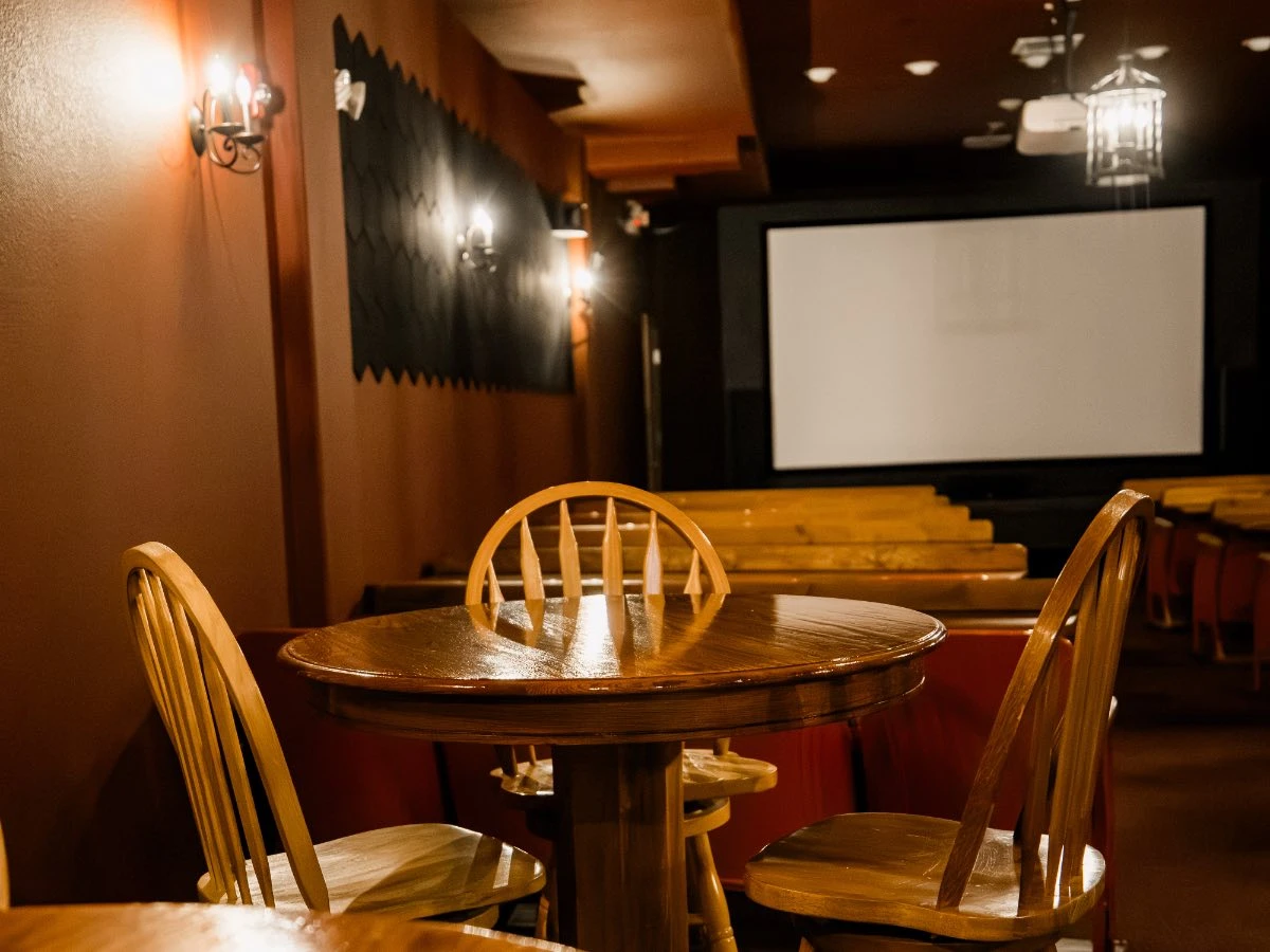 Rear view of Hot Lake Springs Resort theater, row seating in front and tall round tables with chairs for dining in back.