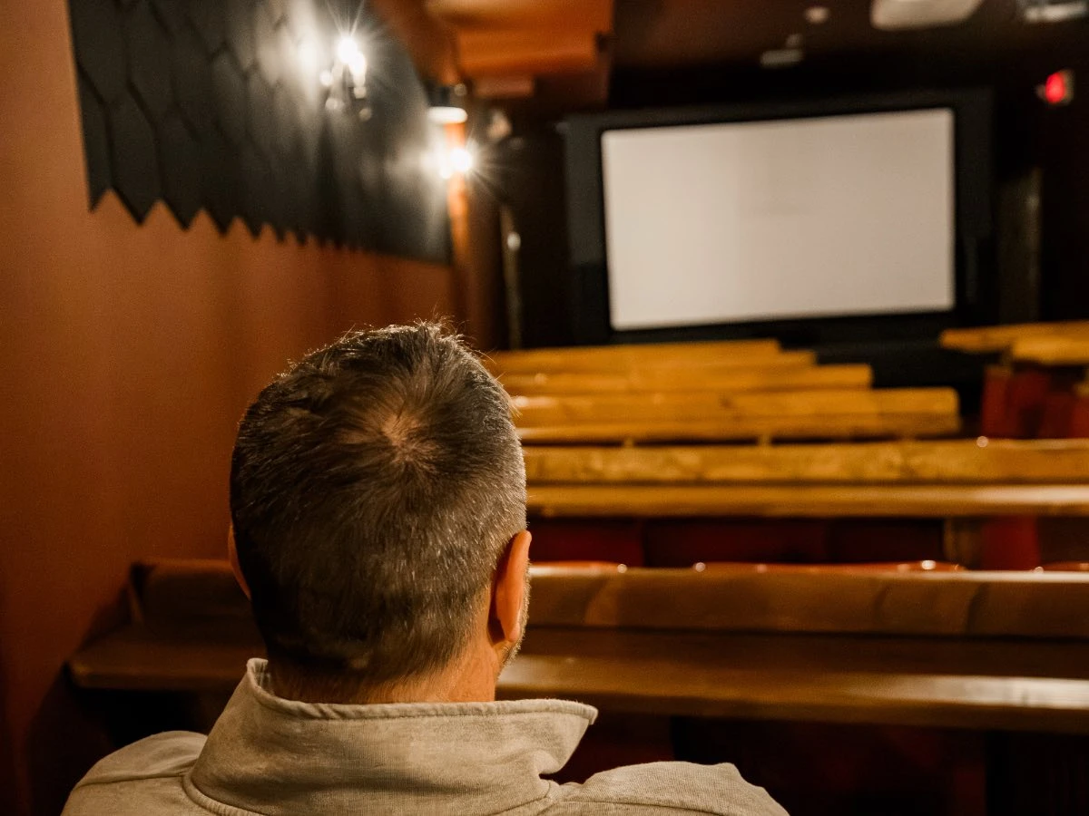 View from behind a guest seated in Hot Lake Springs Resort theater, lights up and blank screen before the film starts.